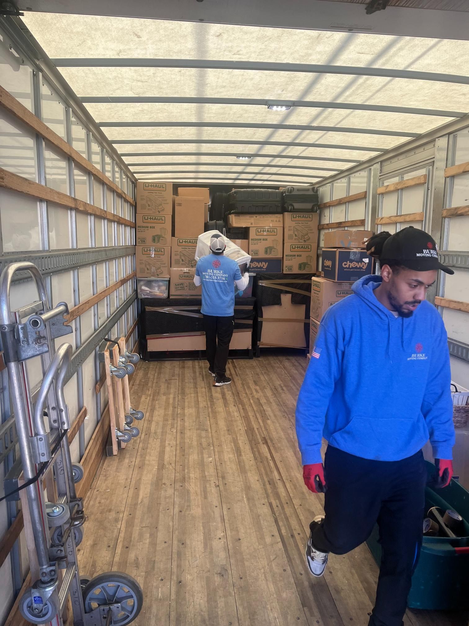 A man in a blue sweatshirt is standing in the back of a moving truck.