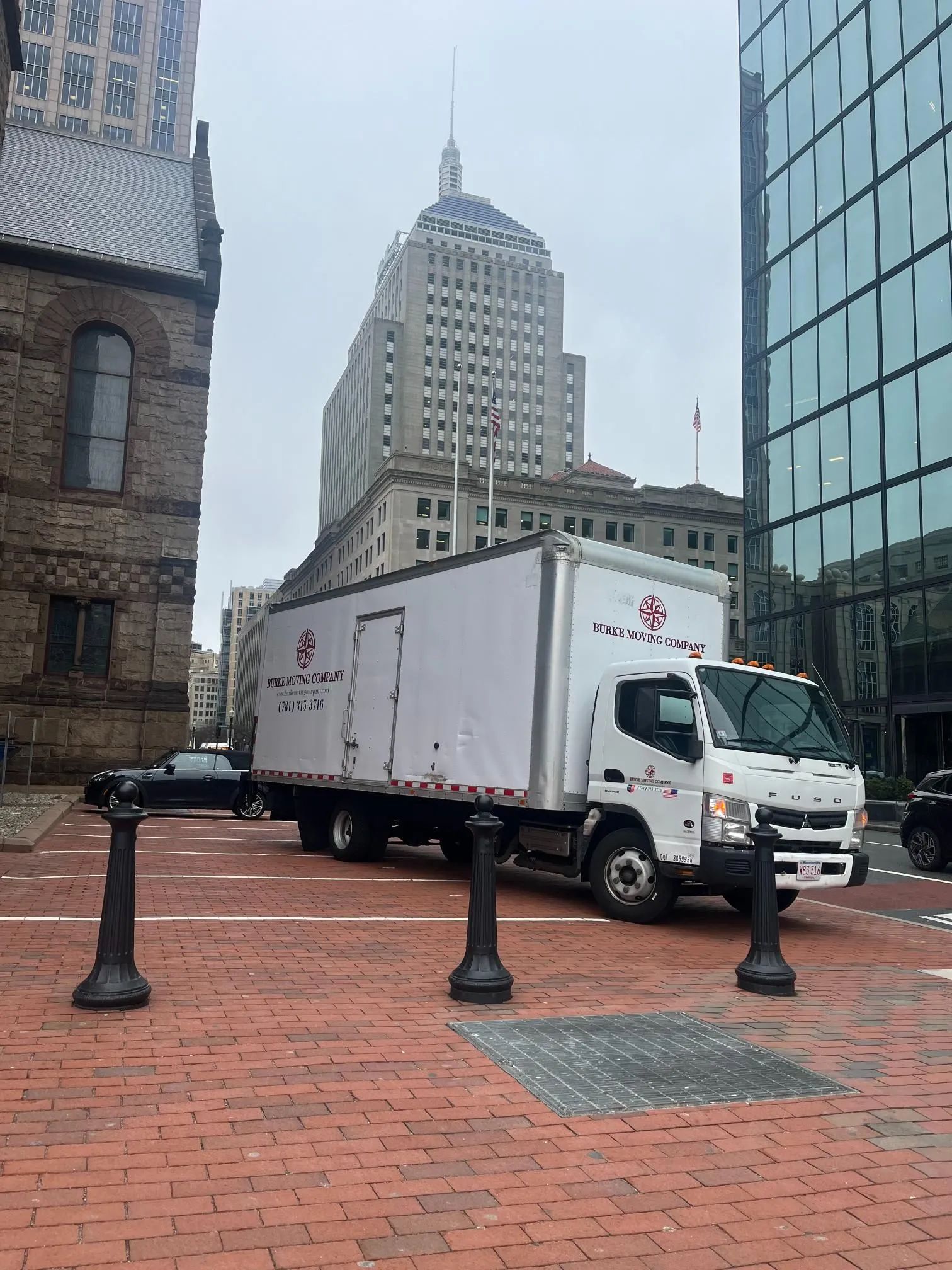 Box truck parked on brick street, with tall buildings in background.