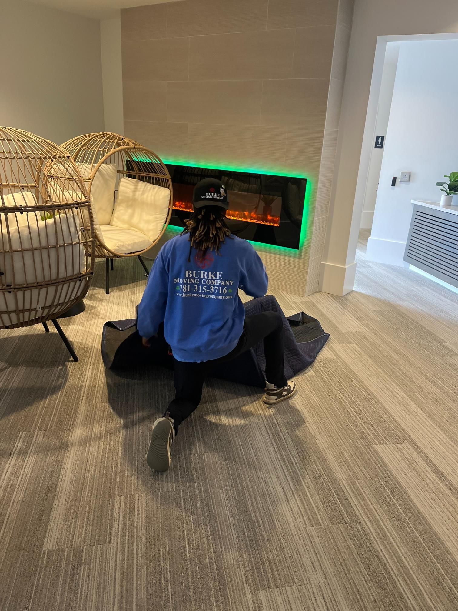 A person is sitting on the floor in a living room next to a fireplace.