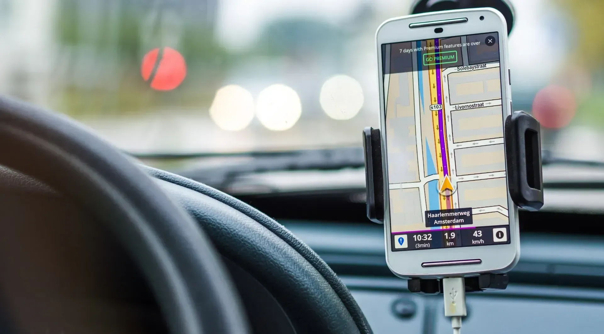 A cell phone is sitting on the steering wheel of a car.