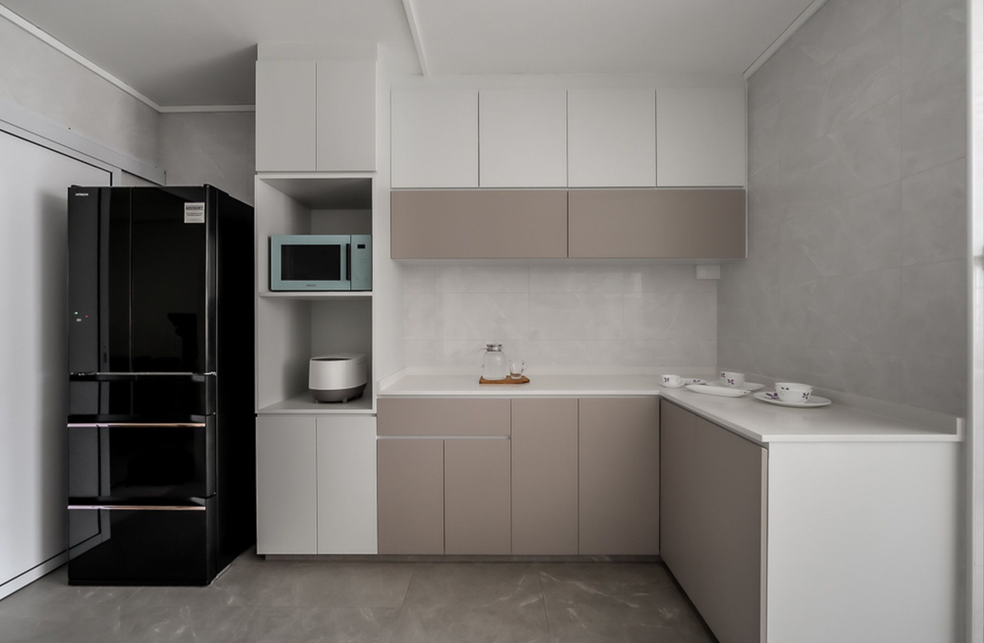 A kitchen with a black refrigerator , white cabinets , and a microwave.