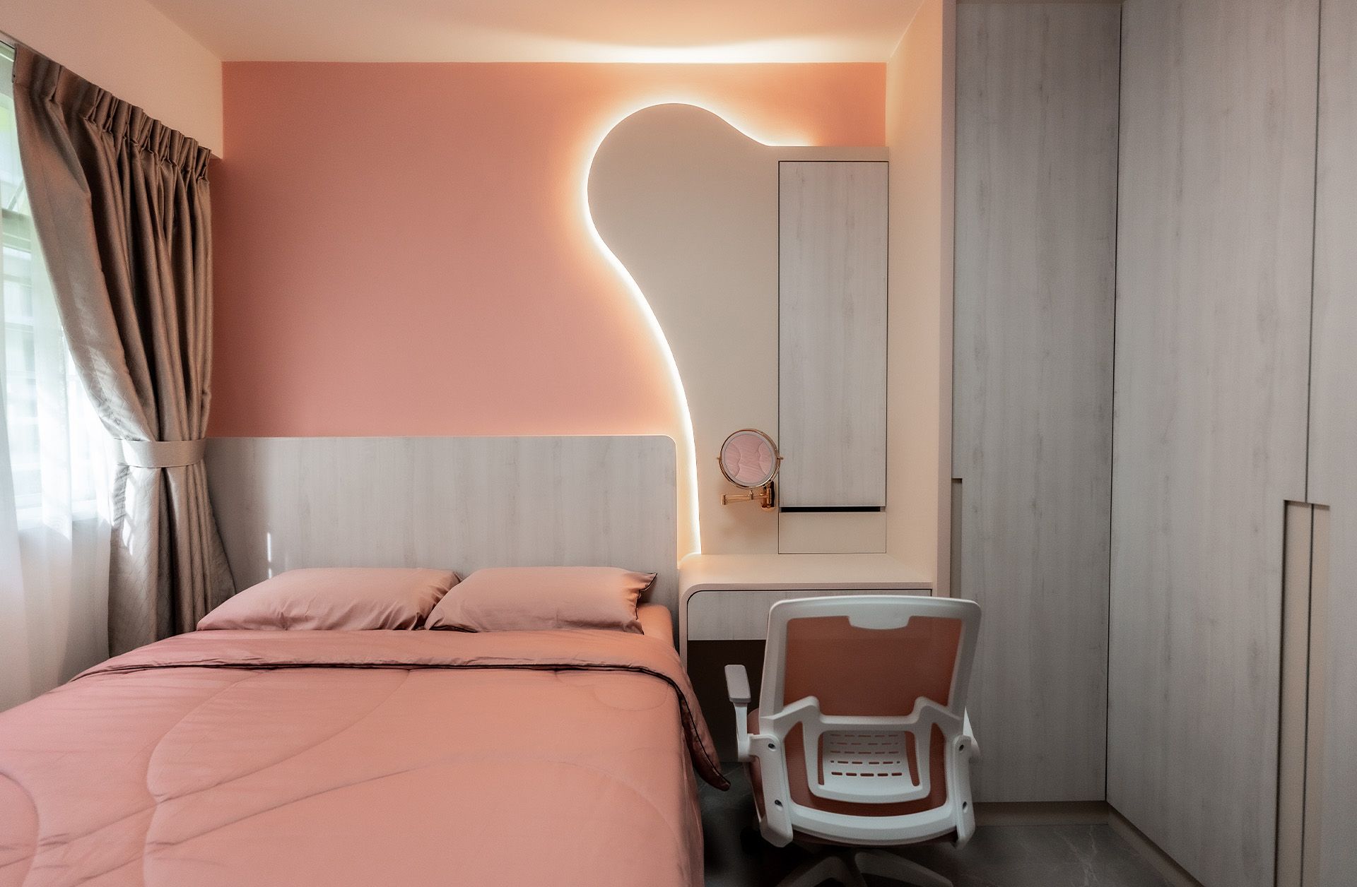 A bedroom with a bed , desk , chair and pink walls.