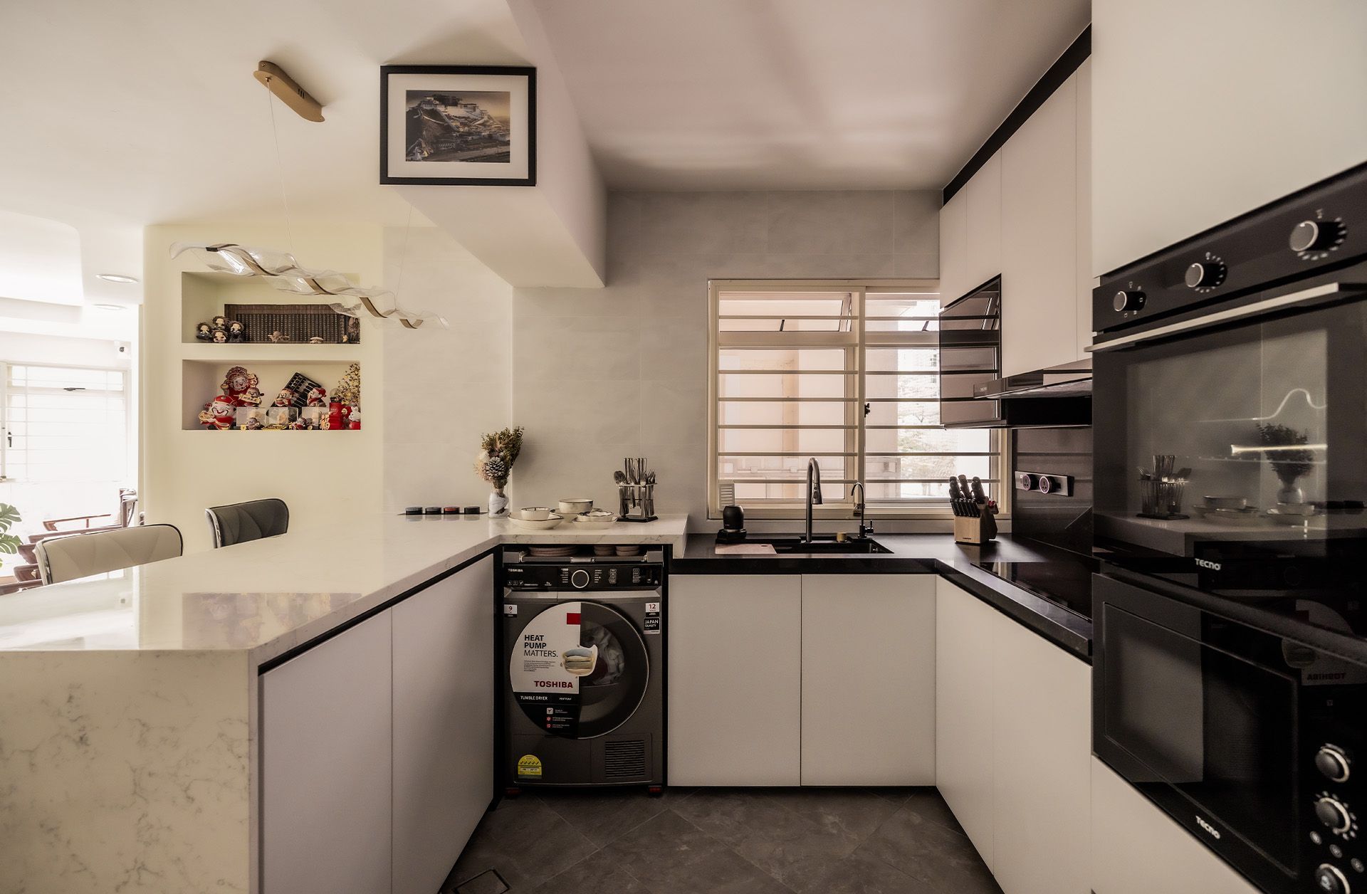 A kitchen with white cabinets , black appliances , a washer and dryer , and a window.