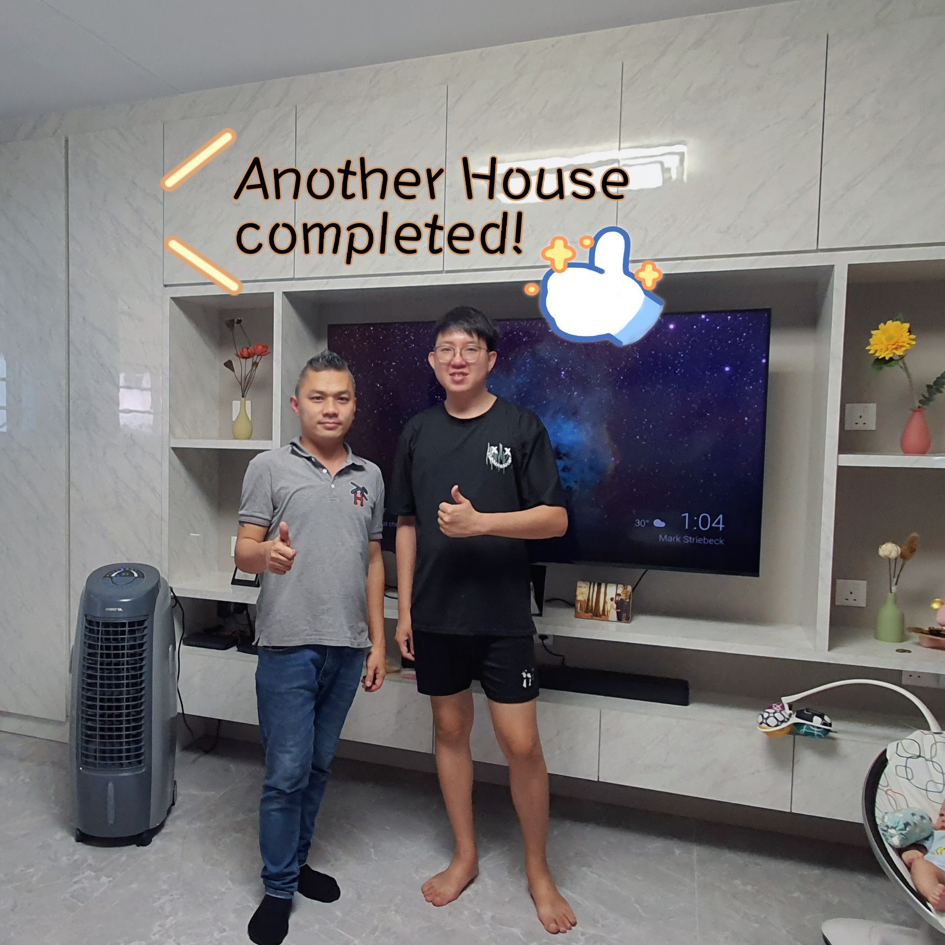 Two men standing in front of a wall that says another house completed