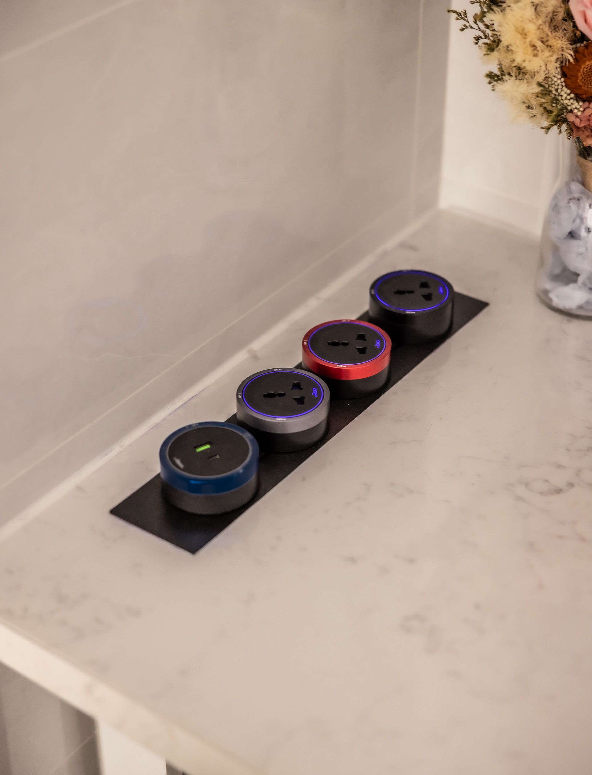 A row of electrical outlets on a counter next to a vase of flowers.