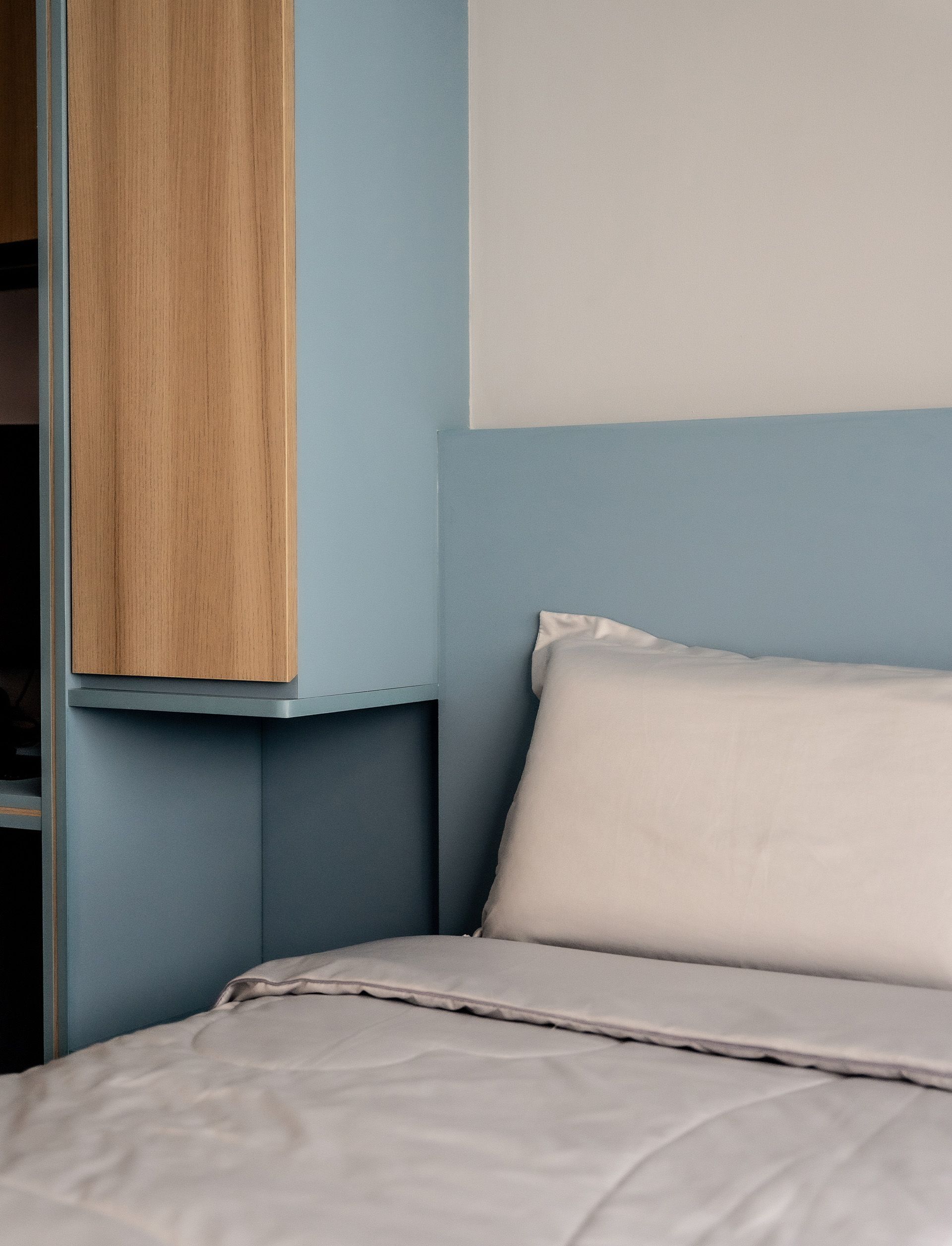 A bed with white sheets and pillows in a bedroom with a blue wall.