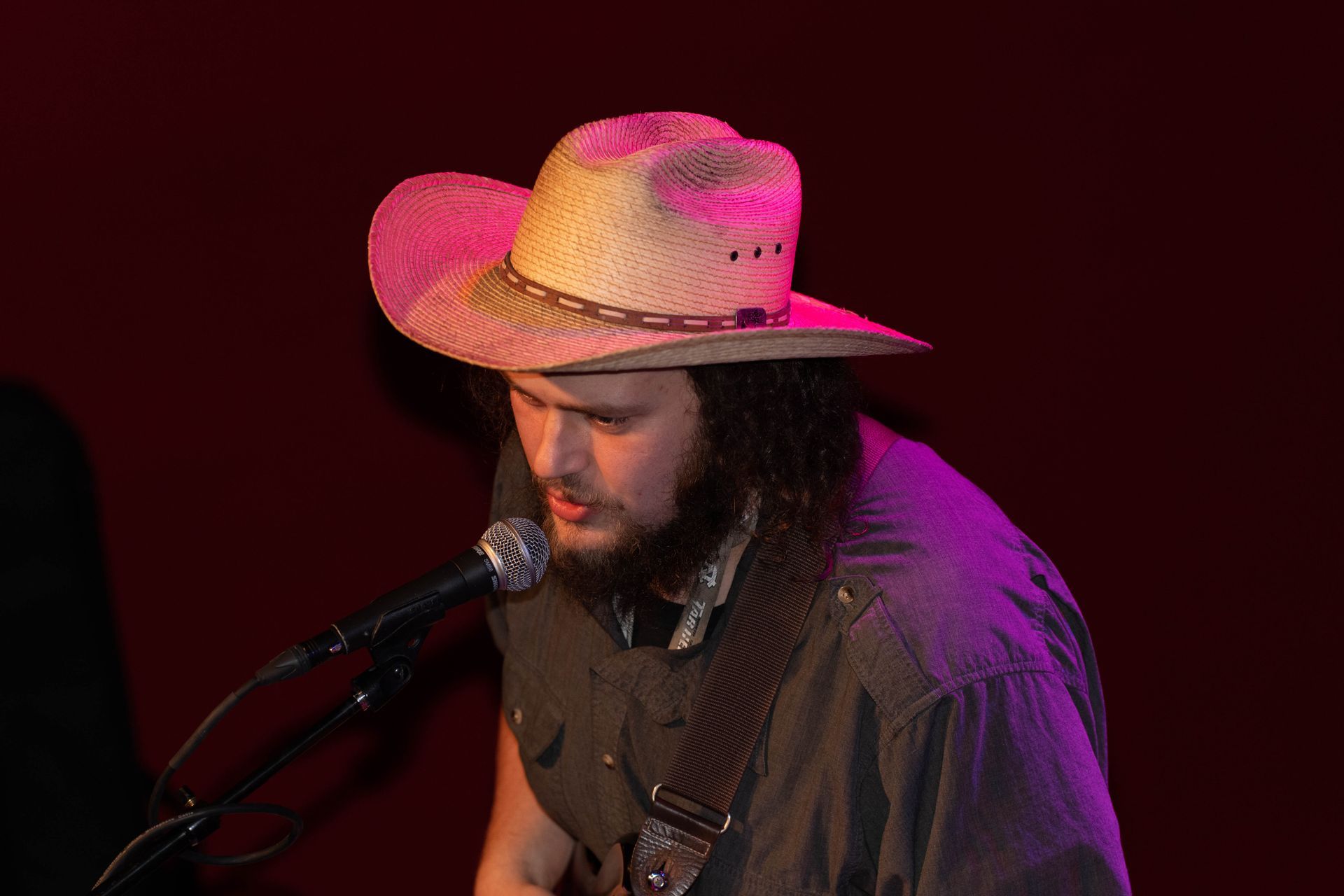 Man in cowboy hat singing into a microphone, lit by pink and purple light.