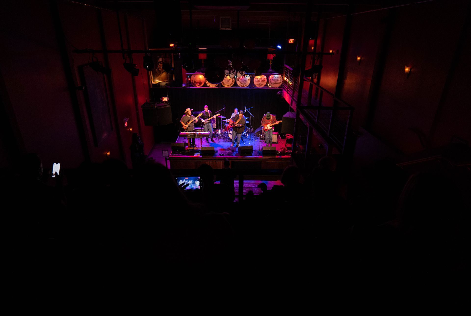 Band performing on stage under colorful lights; audience in dark venue.
