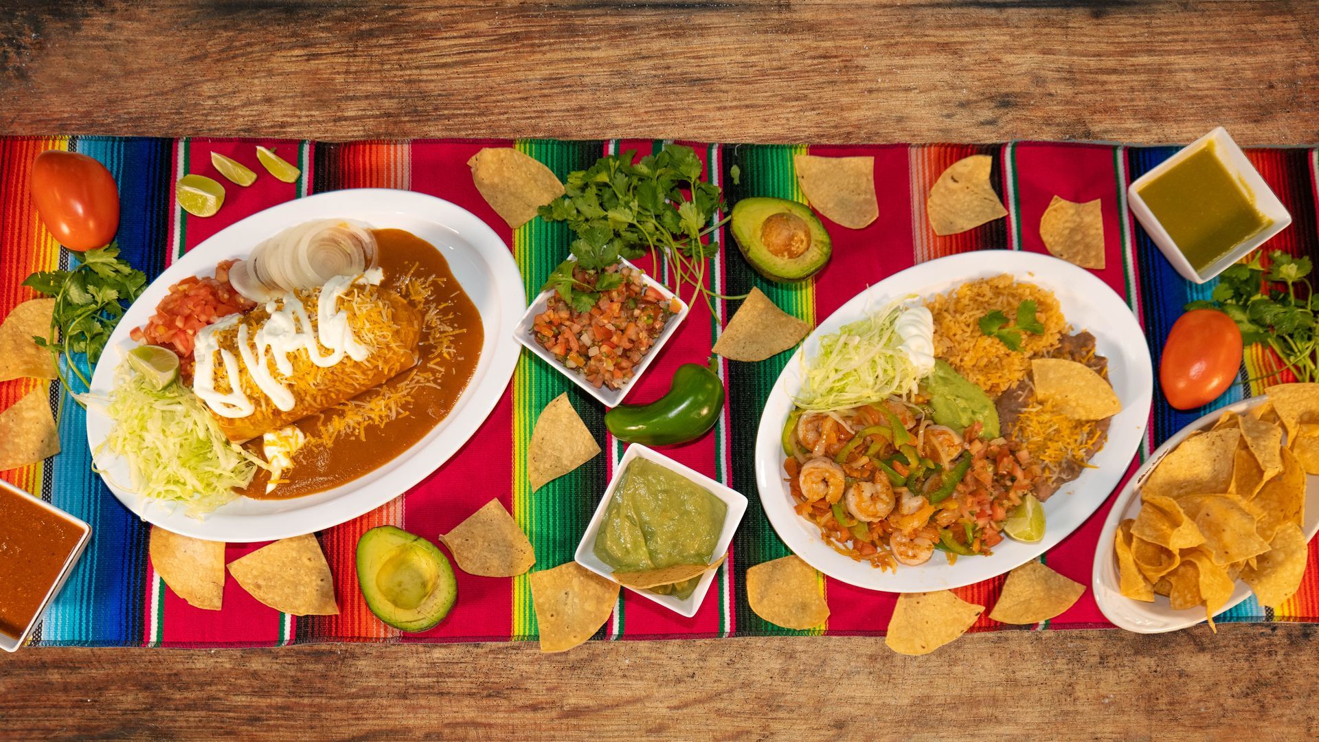 Two plates of Mexican food with toppings, chips, salsa, avocado, and cilantro on a colorful cloth.