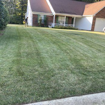 A man is mowing a lush green lawn in front of a house.