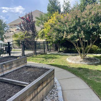 A walkway leading to a garden with raised beds and a fence.