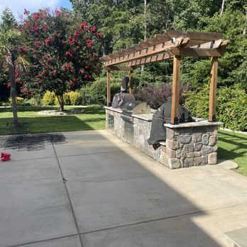 A patio with a grill and a pergola in the backyard.