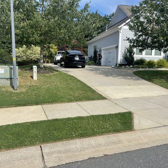 A black car is parked in a driveway next to a white house.