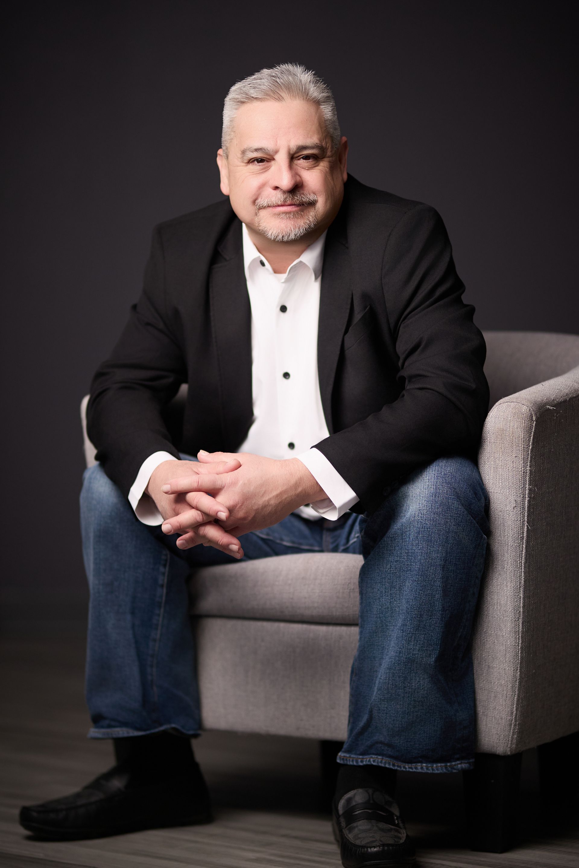 A man in a suit is sitting in a chair and smiling.
