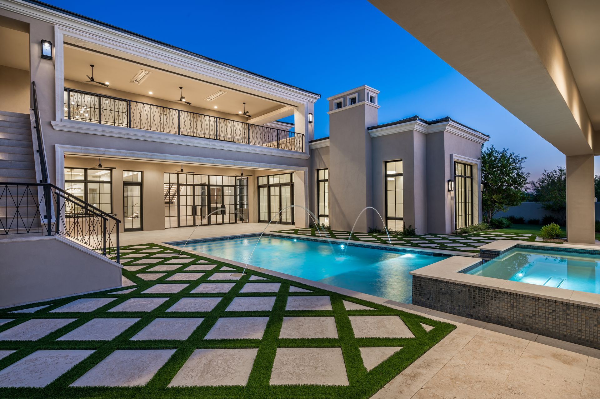 Modern desert luxury house with lit patio, reflecting pool, and paved courtyard at dusk