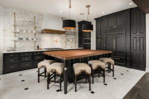 A kitchen with black cabinets , a wooden table and stools.