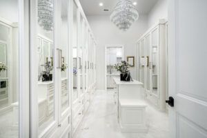 A walk in closet with lots of white cabinets and a chandelier.