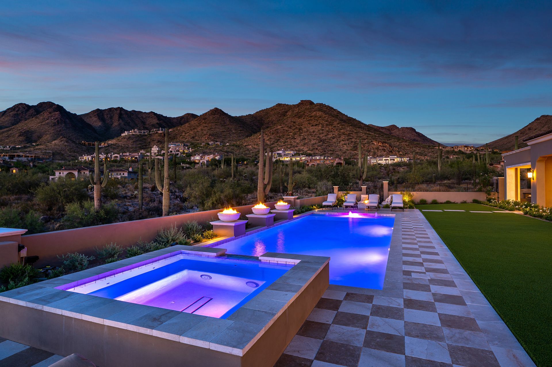 A large swimming pool with a hot tub in the backyard of a house with mountains in the background.