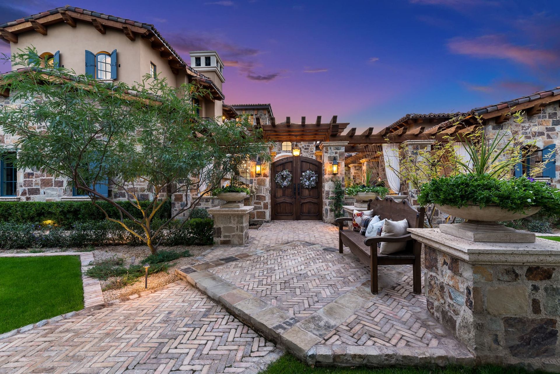 A large stone house with a brick walkway and a bench in front of it.