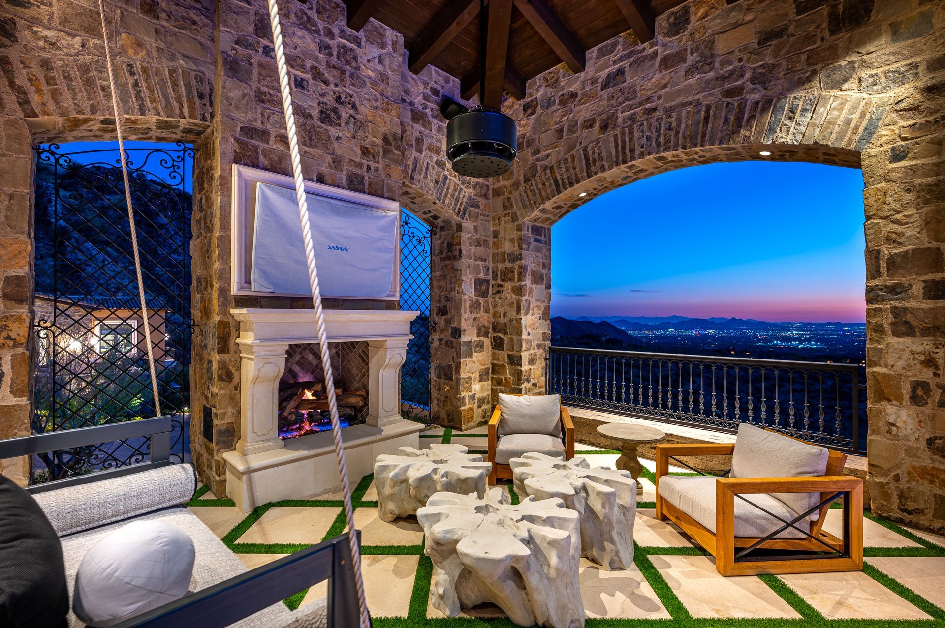A patio with a fireplace , chairs , tables and a swing.