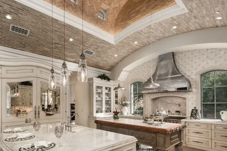 Luxury custom kitchen featuring a vaulted brick ceiling, marble island, & handcrafted cabinetry