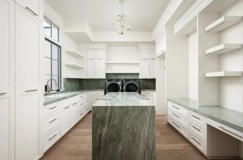 Luxury laundry room with marble island, white cabinets, and modern appliances