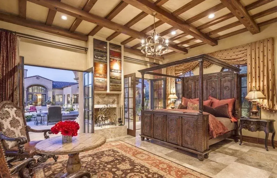 A bedroom with a canopy bed , a table , chairs and a fireplace.