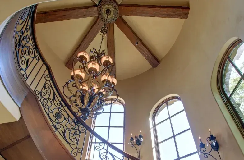 Ornate staircase with a large chandelier in a tall, light-colored room.