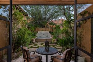 A patio with a table and chairs and a fountain in the background.