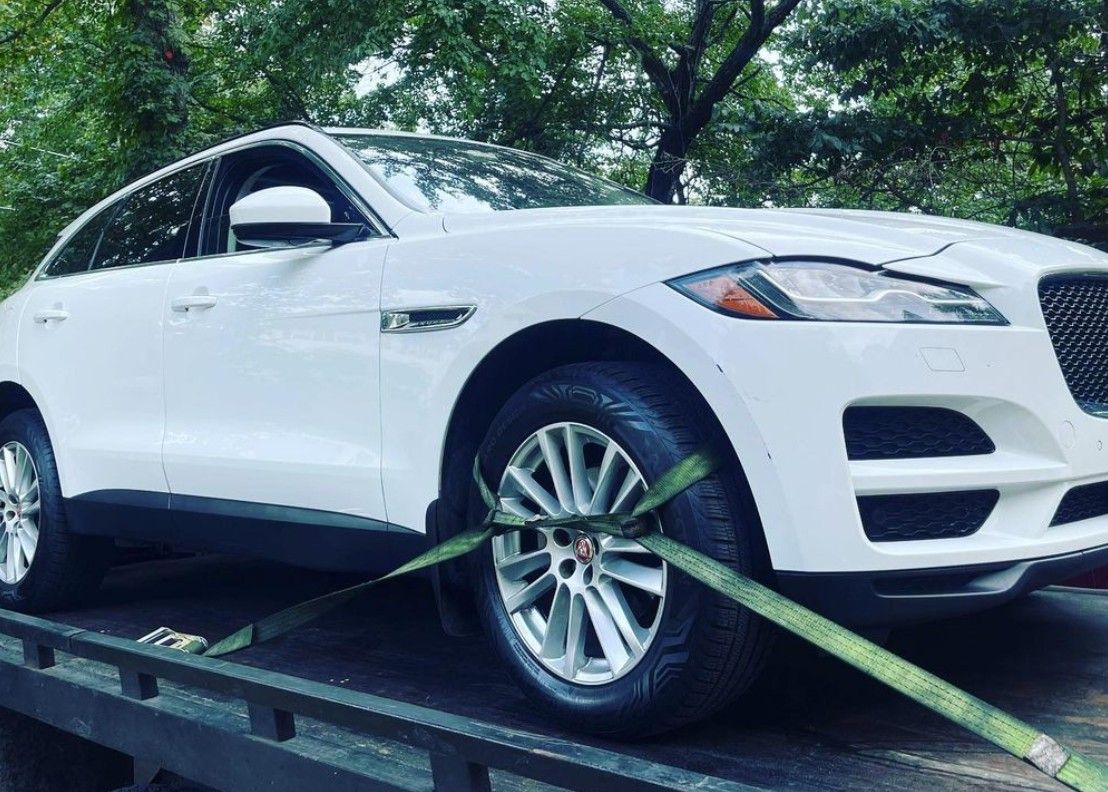 A white car being towed onto a flatbed tow truck on a road, sunny day.