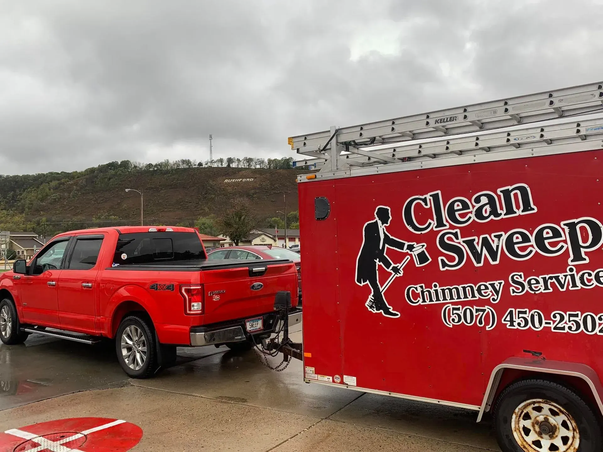 A red truck is parked next to a red trailer that says clean sweep chimney service