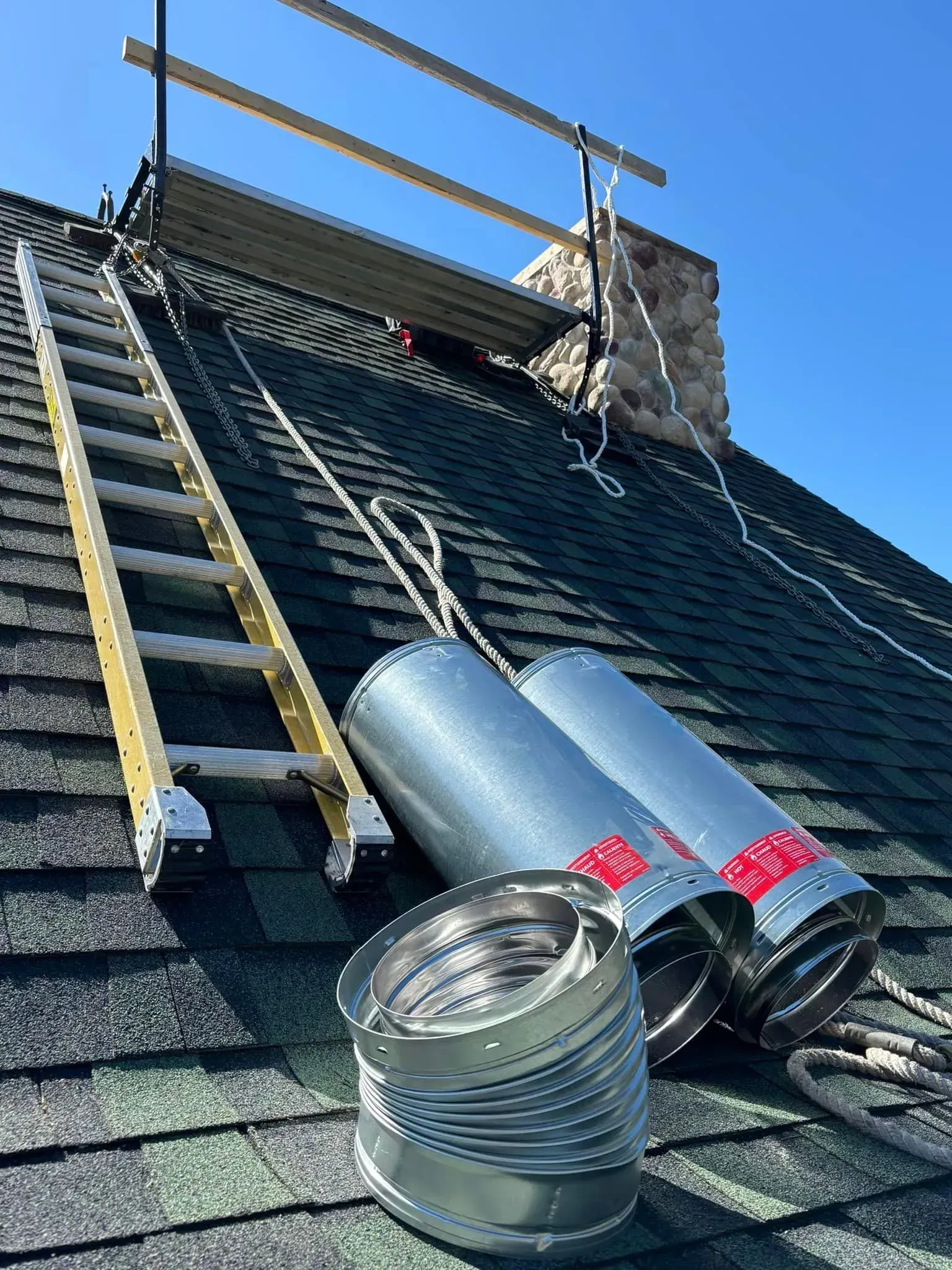 A ladder is sitting on top of a roof next to a chimney.