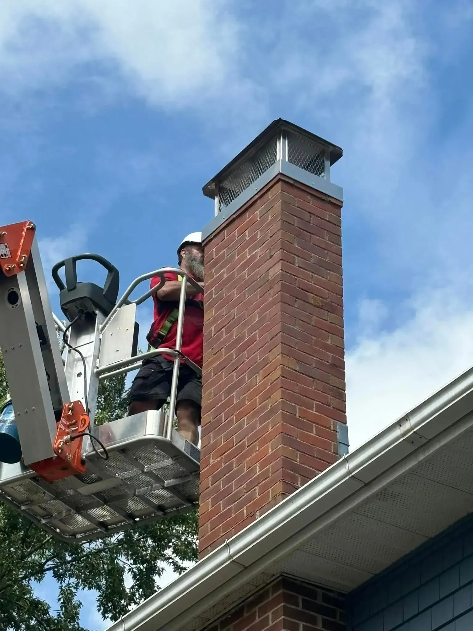 A man is standing on a ladder on top of a brick chimney.