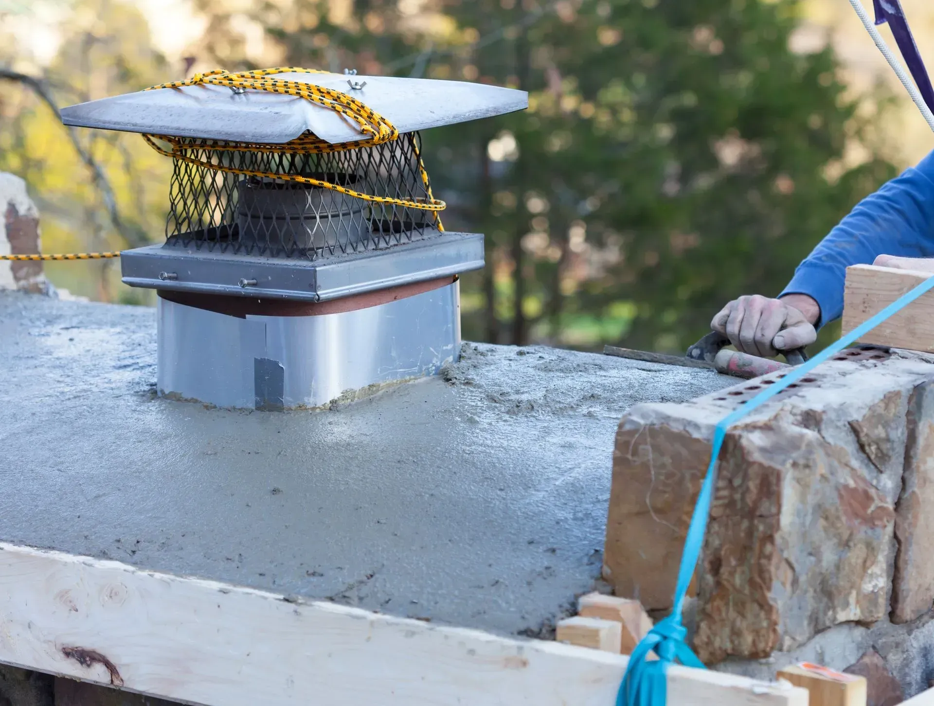 A man is working on a chimney on top of a stone wall.