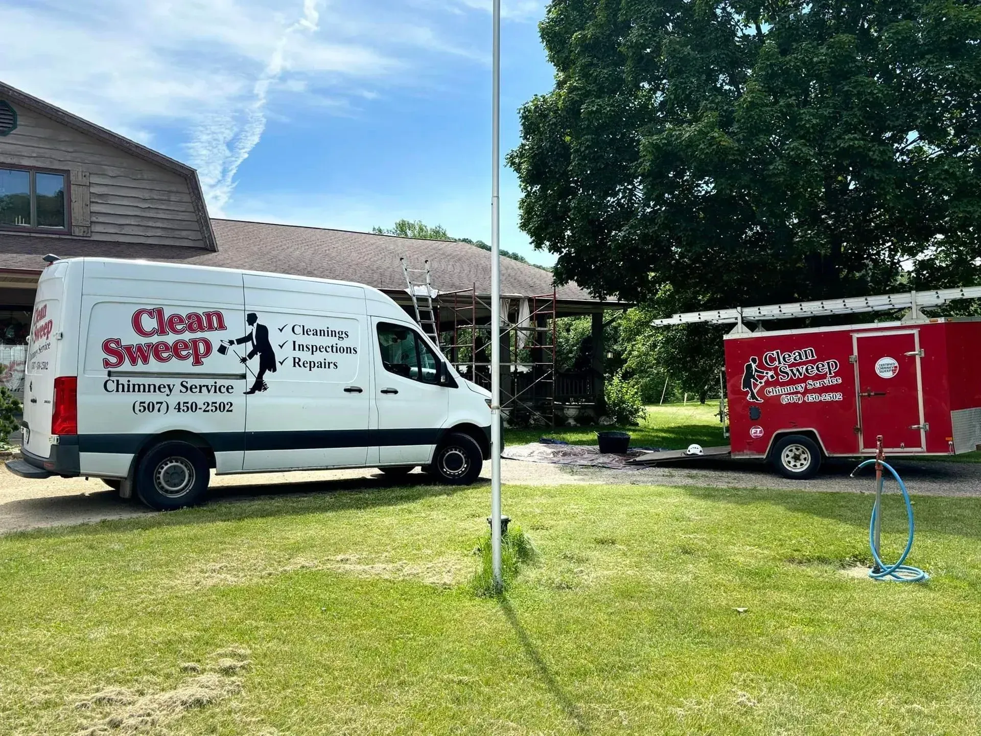 A white van is parked in front of a house next to a red trailer.