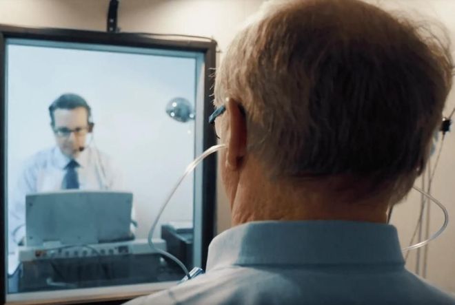 Person viewed on a video call with a doctor in a white coat on a monitor