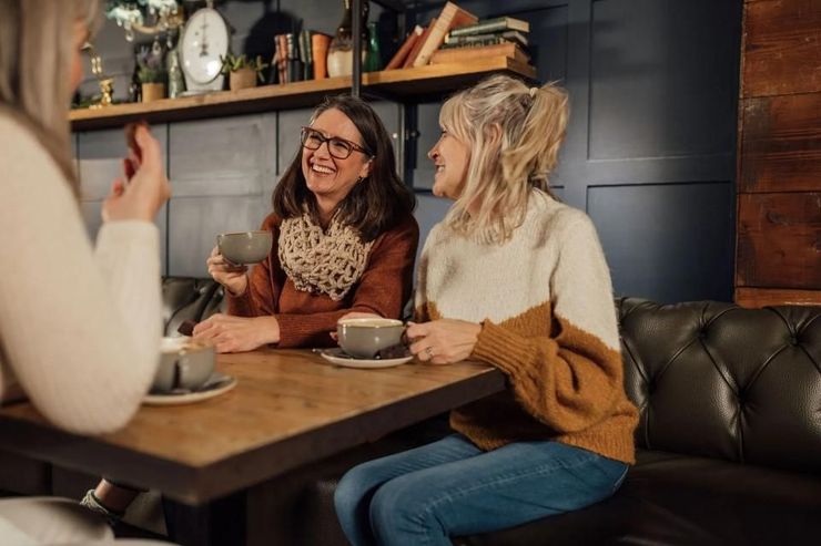 Two friends smiling at a café table, holding coffee cups in a cozy booth.
