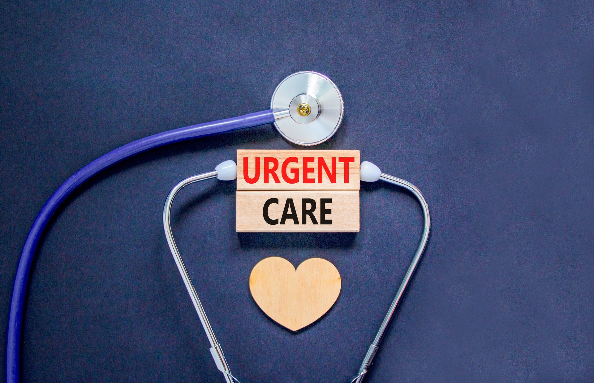 Urgent care sign made of wooden blocks, stethoscope, and wooden heart on a dark blue surface.
