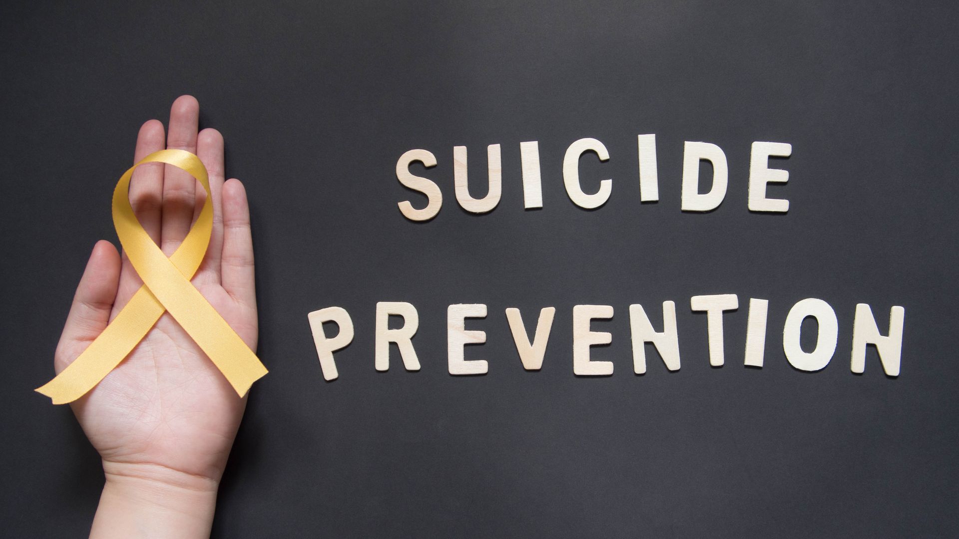 Hand holding a yellow awareness ribbon next to the words 