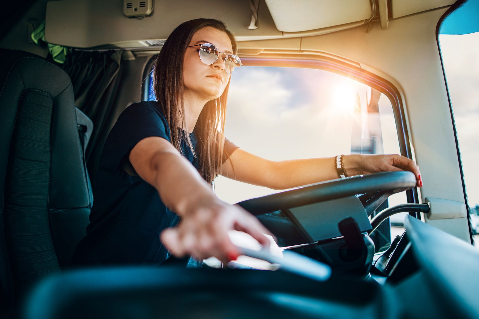 Woman driving a truck, looking forward, hands on the steering wheel, bright sunlight.