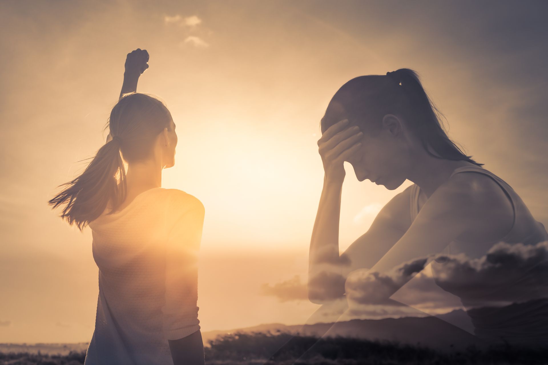 Woman with fist raised in triumph, silhouetted over a sad woman, against a bright sunset.