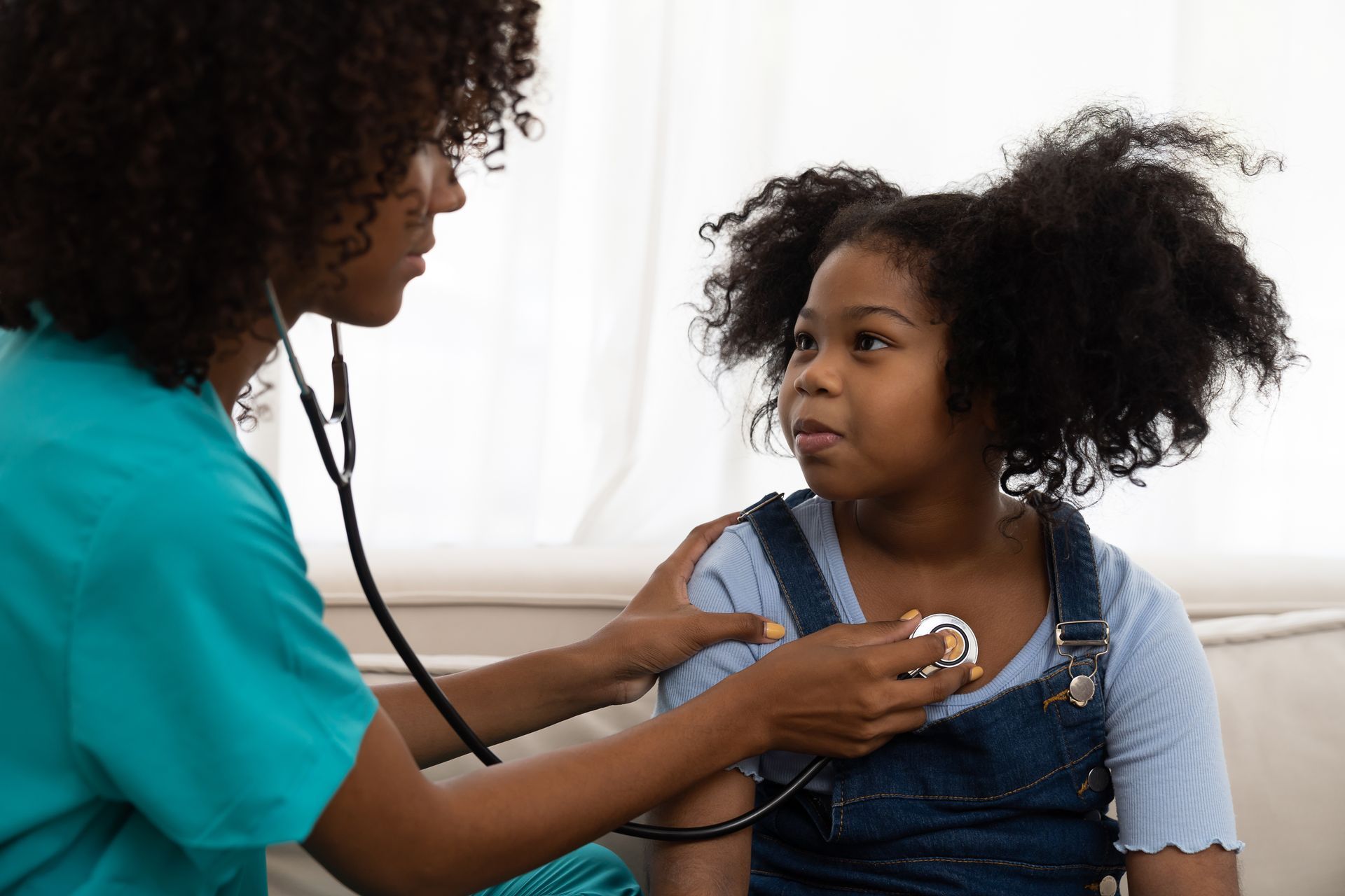 A healthcare professional listening to a young person's chest with a stethoscope.