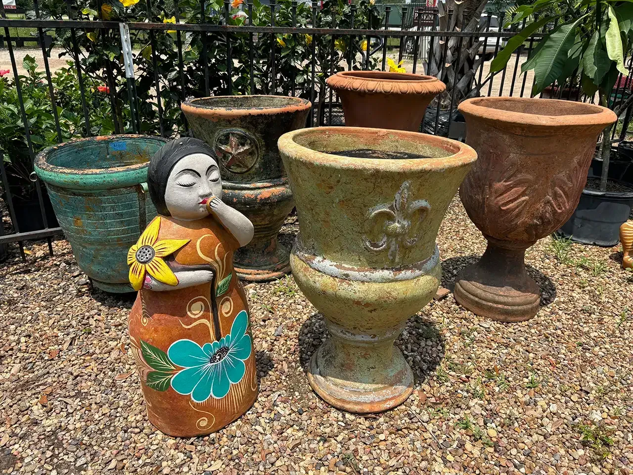 Statue and several weathered urn-shaped planters on gravel.