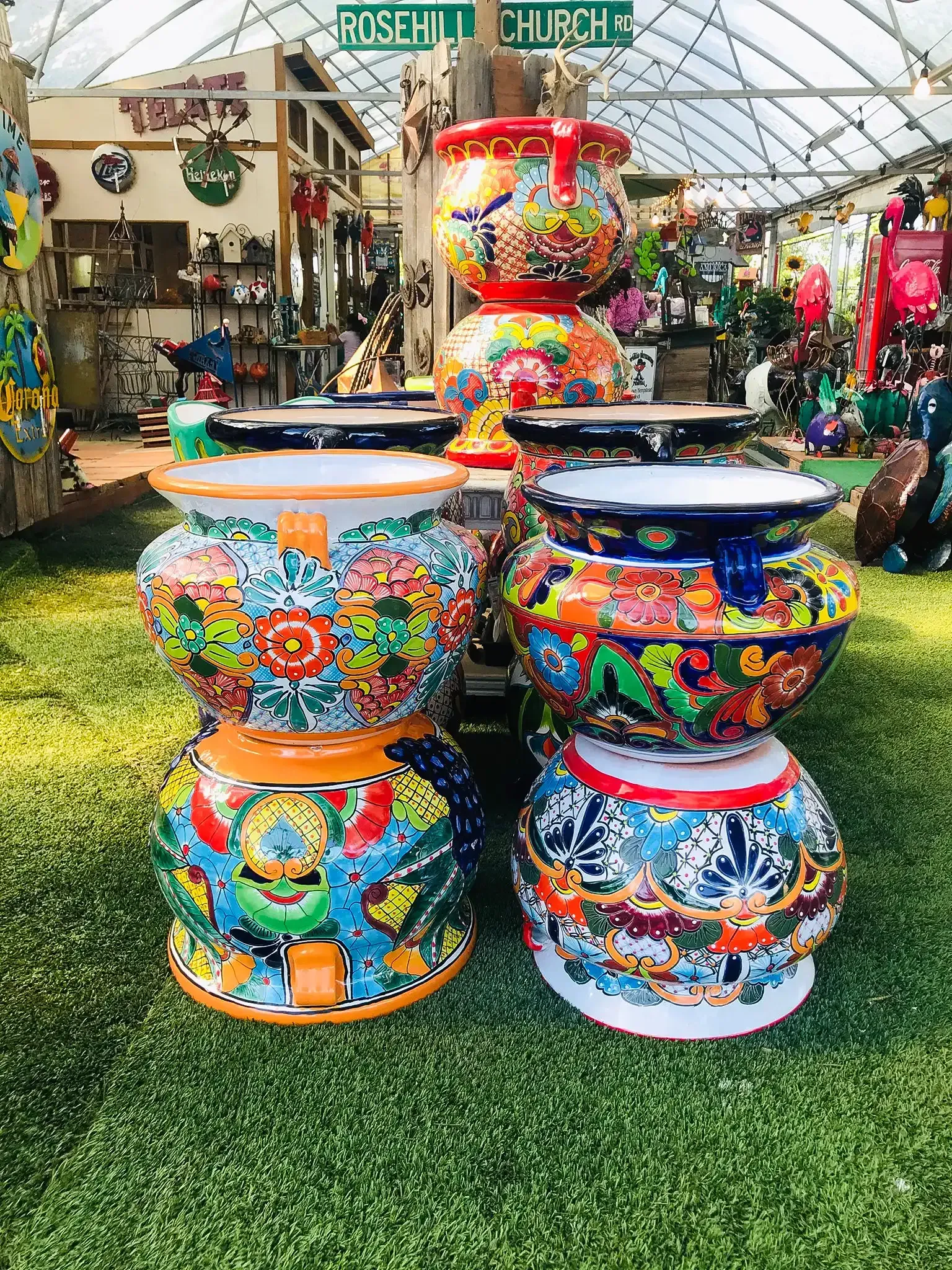 Colorful, patterned ceramic pots stacked in a garden setting, with plants and shop in background.