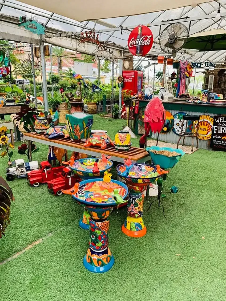 Outdoor market display with colorful pottery, signs, and decor under a canopy.