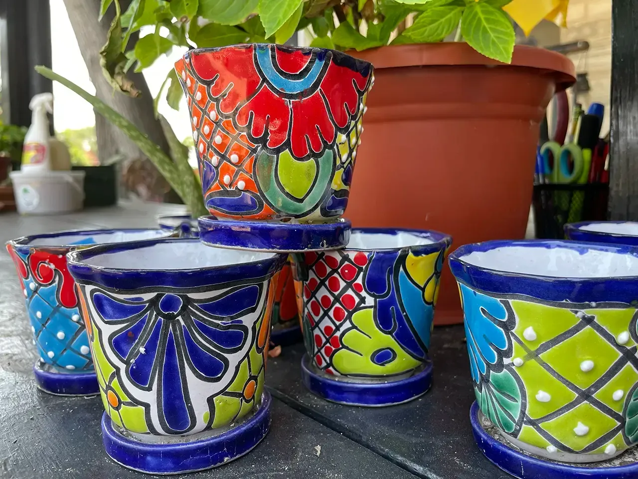 Colorful, decorative ceramic plant pots with blue trim and saucers; several stacked on a wooden surface