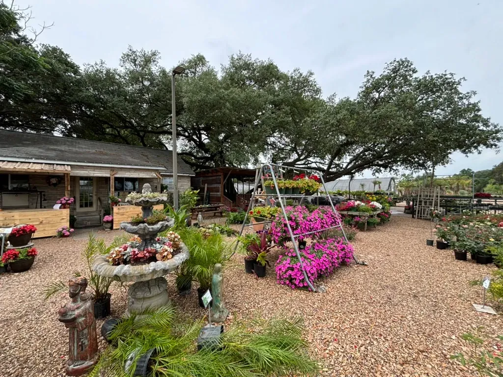 A garden center with flowers, fountains, and a building under a cloudy sky.
