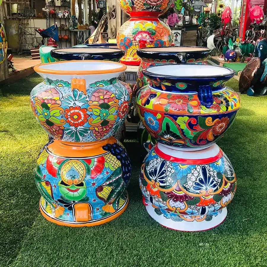 Colorful, ceramic flower pots stacked outside. Floral patterns, blue rims, and vibrant colors on green grass.