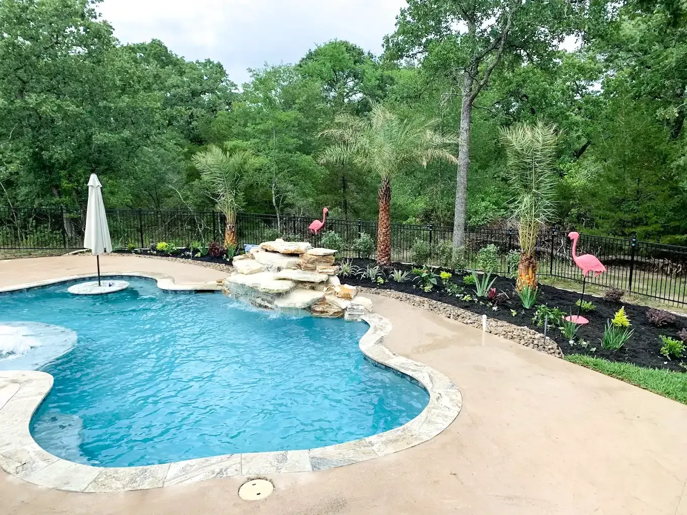 Swimming pool with a rock waterfall and landscaping, featuring pink flamingo decorations.
