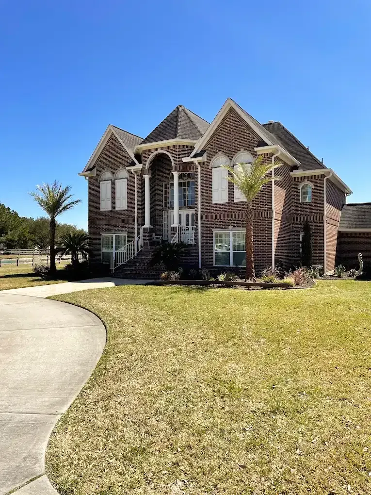 Brick house with a curved driveway and manicured lawn under a clear blue sky.